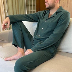 K&ouml;nnte beinhalten: Eine Person tr&auml;gt einen dunkelgr&uuml;nen, lang&auml;rmeligen Schlafanzug-Oberteil und eine passende Hose. Der Schlafanzug hat einen Knopfleistenverschluss und einen Kragen.