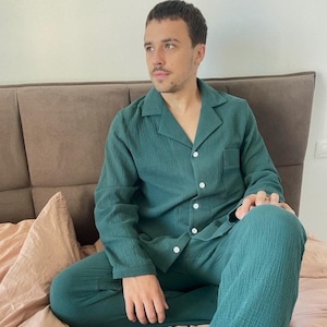 K&ouml;nnte beinhalten: Eine Person tr&auml;gt einen gr&uuml;nen Schlafanzug mit einem Hemd mit Kragen und einer langen Hose. Die Person sitzt auf einem Bett mit einer rosa Decke.