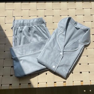 K&ouml;nnte beinhalten: Ein hellblauer Pyjama-Set mit einem Hemd mit Kragen und einer Hose. Das Hemd hat einen wei&szlig;en Saum um den Kragen und die &Auml;rmelb&uuml;ndchen. Die Hose hat einen wei&szlig;en Saum am unteren Rand.