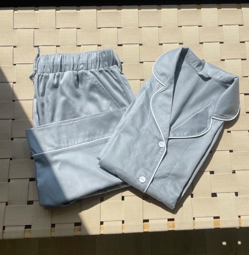 K&ouml;nnte beinhalten: Ein hellblauer Pyjama-Set mit einem Hemd mit Kragen und einer Hose. Das Hemd hat einen wei&szlig;en Saum um den Kragen und die &Auml;rmelb&uuml;ndchen. Die Hose hat einen wei&szlig;en Saum am unteren Rand.