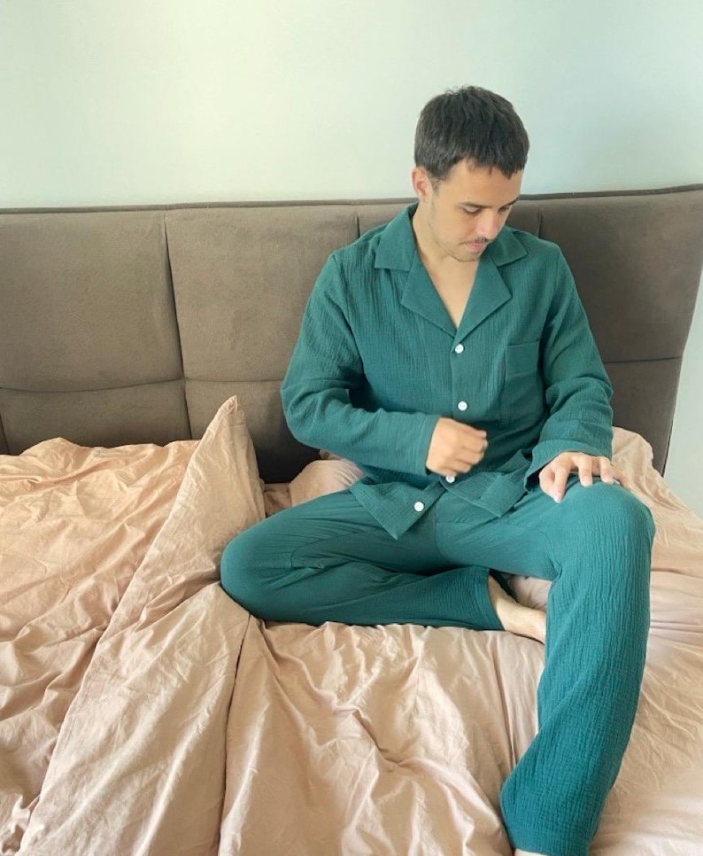 K&ouml;nnte beinhalten: Eine Person tr&auml;gt einen gr&uuml;nen Waffelpiqu&eacute;-Pyjama mit einem Hemd mit Kn&ouml;pfen und einer langen Hose. Die Person sitzt auf einem Bett mit einem braunen Kopfteil und einer rosa Bettdecke.