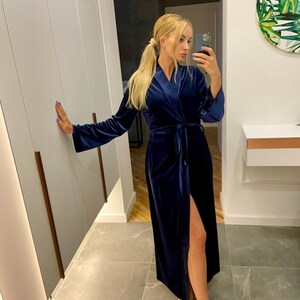 May include: A long, dark blue velvet robe with a tie belt and a side slit. The robe is worn by a person with long blonde hair.