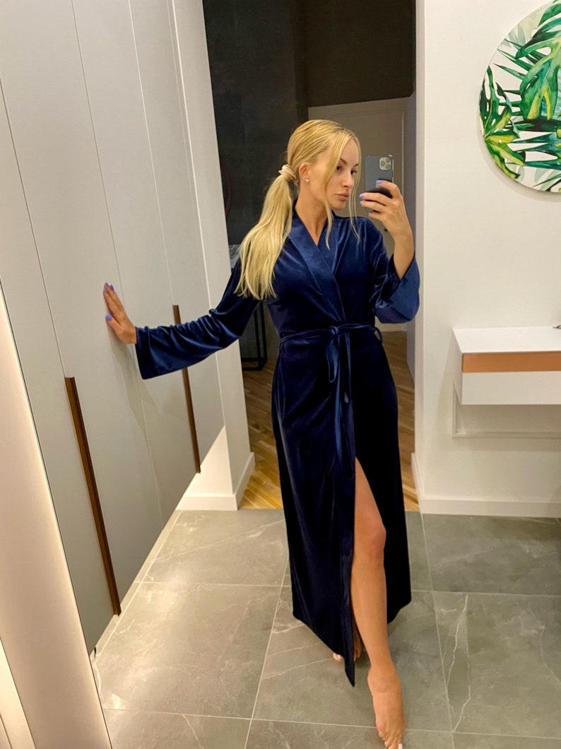 May include: A long, dark blue velvet robe with a tie belt and a side slit. The robe is worn by a person with long blonde hair.