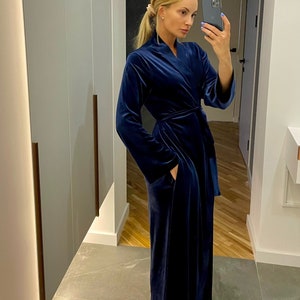 May include: A long, dark blue velvet robe with a shawl collar and a tie belt. The robe has pockets on the sides.