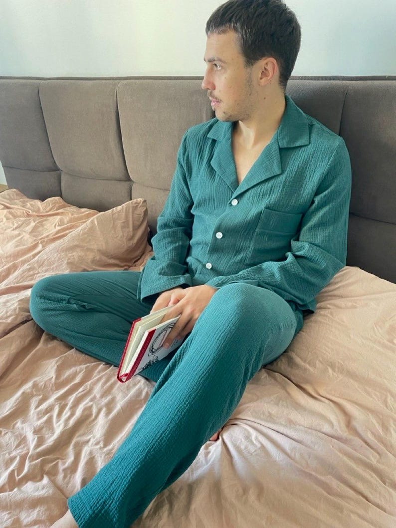 K&ouml;nnte beinhalten: Eine Person tr&auml;gt einen tealblauen Schlafanzug mit einem lang&auml;rmeligen Hemd und einer Hose. Die Person sitzt auf einem Bett und h&auml;lt ein Buch.