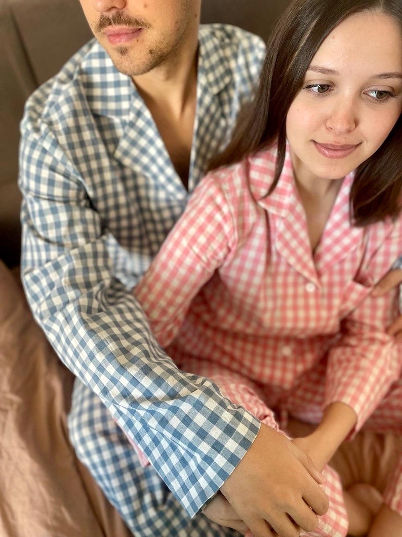 Puede incluir: Una pareja vistiendo pijamas a juego de cuadros azules y rosas. El hombre lleva una camisa de pijama de cuadros azules y la mujer lleva una camisa de pijama de cuadros rosas.