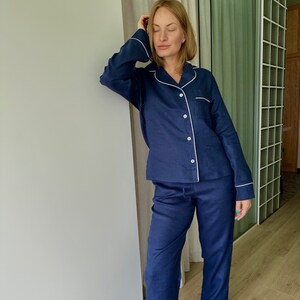 May include: A navy blue pajama set with white piping. The top has a long sleeve and a button-up front. The pants are long and have a straight leg.