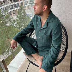 K&ouml;nnte beinhalten: Eine Person tr&auml;gt ein gr&uuml;nes, lang&auml;rmliges Pyjama-Oberteil und eine passende Hose. Der Pyjama-Satz hat einen Knopfleisten vorne und eine Tasche auf der linken Seite des Oberteils.