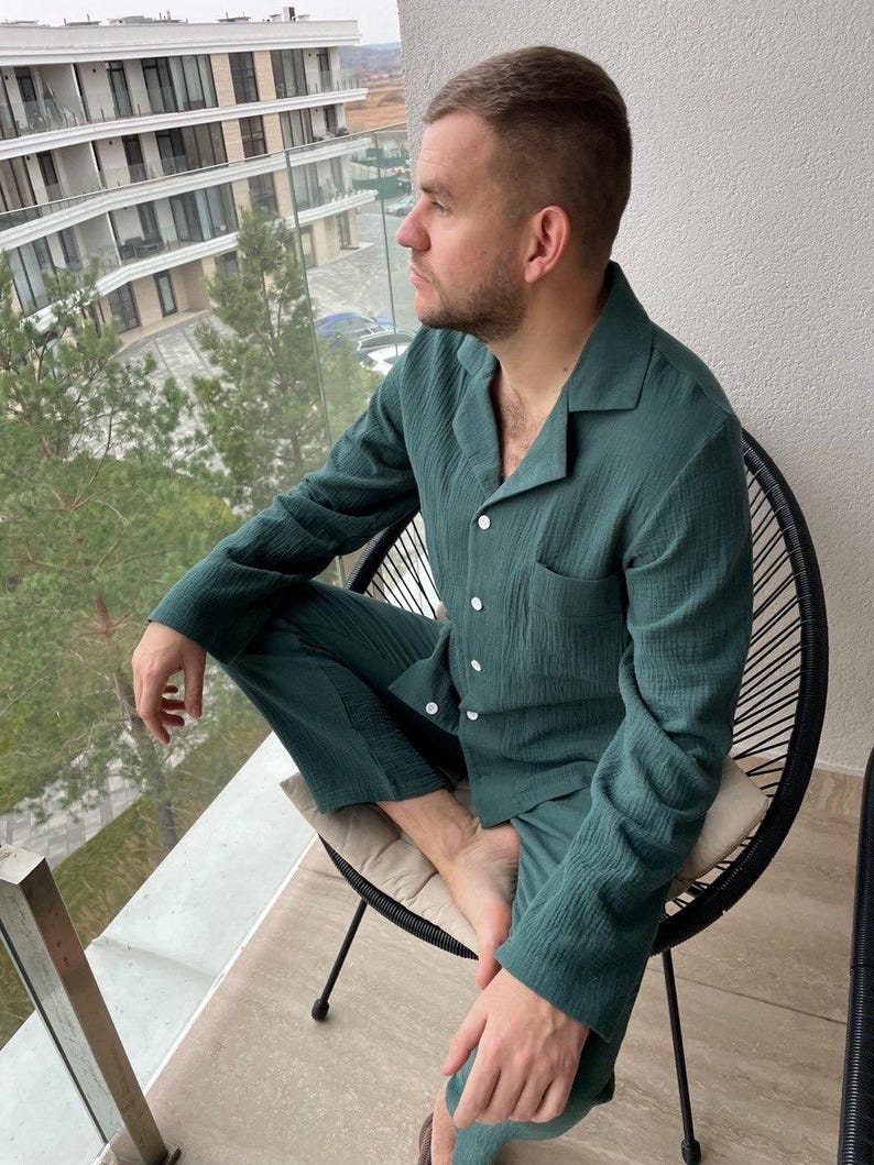 K&ouml;nnte beinhalten: Eine Person tr&auml;gt ein gr&uuml;nes, lang&auml;rmliges Pyjama-Oberteil und eine passende Hose. Der Pyjama-Satz hat einen Knopfleisten vorne und eine Tasche auf der linken Seite des Oberteils.