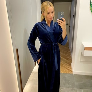 May include: A long, dark blue velvet robe with a shawl collar and a tie belt. The robe has pockets on the sides.