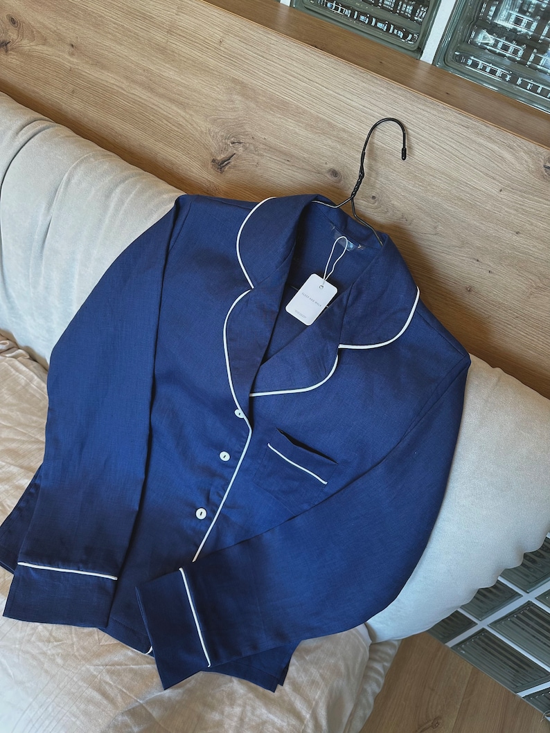 May include: A navy blue long-sleeved pajama top with white piping around the collar, cuffs, and pockets. The top has a button closure and a small white tag with the text "GOODNIGHT" on it.