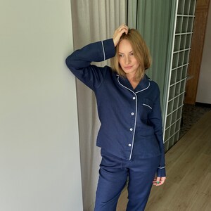 May include: A navy blue pajama set with white piping. The top has a button-down front and long sleeves. The pants have a straight leg and a white trim at the bottom.