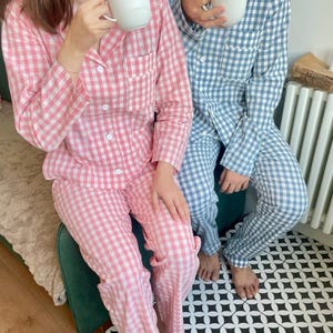 Puede incluir: Dos personas vistiendo pijamas a cuadros a juego. Una persona lleva un pijama a cuadros rosa y blanco y la otra lleva un pijama a cuadros azul y blanco. Ambas personas sostienen tazas blancas.