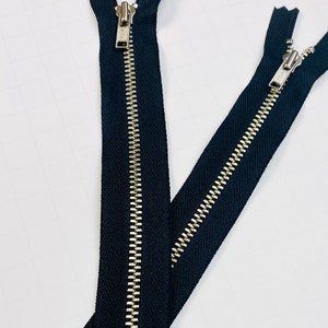 May include: Two black zipper closures with silver metal teeth. The zippers are laid out in a criss-cross pattern.