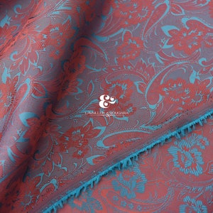 Può includere: Tessuto rosso e turchese con un motivo paisley. Il tessuto ha una superficie testurizzata e un bordo con frange.