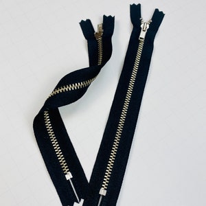 May include: Two black zipper closures with gold metal teeth. The zippers are laid out on a white surface.