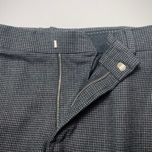 May include: A pair of gray pants with a black and white houndstooth pattern. The pants have a zipper fly and a button closure.