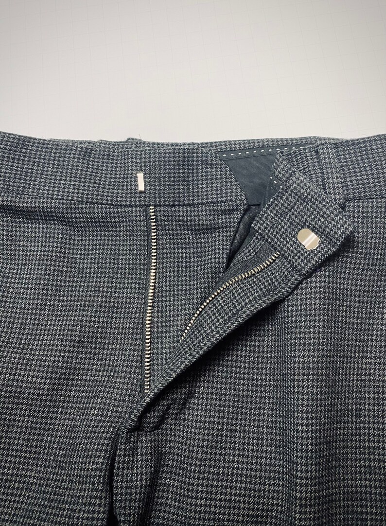 May include: A pair of gray pants with a black and white houndstooth pattern. The pants have a zipper fly and a button closure.