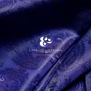 Op de afbeelding: Een close-up van een diepblauwe stof met een paisley-patroon. De stof is doormidden gevouwen en het logo "L'AVAILER & BOUCARA" is zichtbaar in het midden.