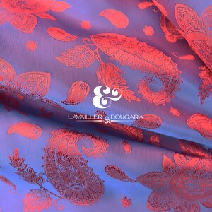 Puede incluir: Primer plano de una tela con un estampado floral y de cachemira. La tela tiene un fondo azul con un dise&ntilde;o floral rojo. La tela est&aacute; doblada, mostrando la textura y profundidad del material. El logotipo "LAVAILLER & BOUGARA" es visible.