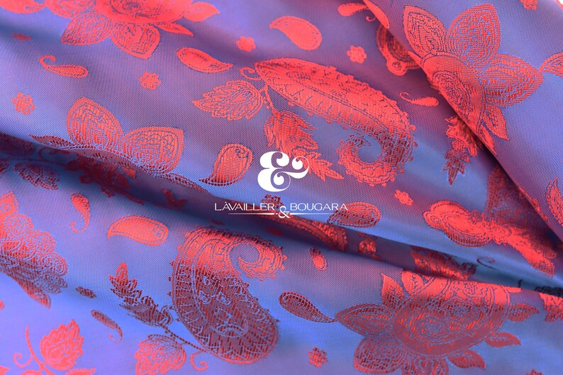 Puede incluir: Primer plano de una tela con un estampado floral y de cachemira. La tela tiene un fondo azul con un dise&ntilde;o floral rojo. La tela est&aacute; doblada, mostrando la textura y profundidad del material. El logotipo "LAVAILLER & BOUGARA" es visible.