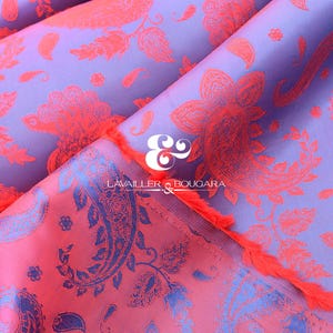 Puede incluir: Primer plano de una tela doblada con un estampado de cachemira. La tela tiene un fondo morado con un dise&ntilde;o floral coral. El borde de la tela tiene una franja coral. El texto "LAVAILLER & BOUGARA" es visible.