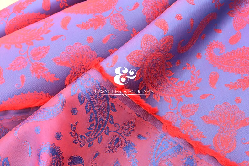 Puede incluir: Primer plano de una tela doblada con un estampado de cachemira. La tela tiene un fondo morado con un dise&ntilde;o floral coral. El borde de la tela tiene una franja coral. El texto "LAVAILLER & BOUGARA" es visible.
