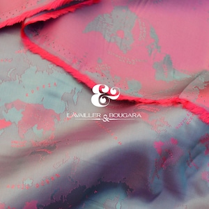 Könnte beinhalten: Nahaufnahme eines Stoffes mit einem kartenartigen Design in Rosa-, Türkis- und Lilatönen. Die Kanten sind mit einem leuchtend pinkfarbenen Fransenband versehen. Der Stoff trägt den weißen Text "LAVAILLER & BOUGARA".