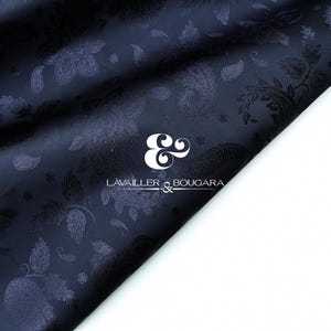 May include: Dark navy blue fabric with a paisley pattern. The fabric is folded, revealing the intricate design of the paisley motifs. The logo "LAVAILLER & BOUGARA" is visible in white. The fabric has a slight sheen.