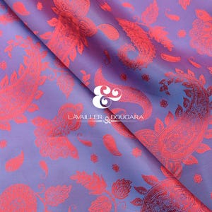 Puede incluir: Una tela doblada con un patr&oacute;n de cachemira coral repetido sobre un fondo lavanda y azul. La tela tiene brillo y los dise&ntilde;os de cachemira son detallados. La marca "LAVALLER & BOUGARA" es visible.