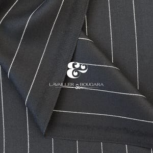May include: Close-up of black fabric with vertical white pinstripes. The fabric is folded, revealing the texture and pattern. The brand name "LAVAILLER & BOUGARA" is visible in white text. This textile is suitable for suiting and other apparel.