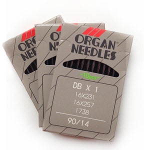 May include: Three gray cardboard packages of Organ Needles, each with a red and black logo. The packages display the text "DB X 1", "16X231", "16X257", "1738", and "90/14". Each package contains 10 needles.