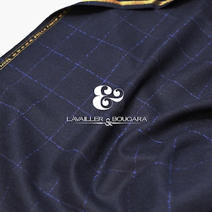 May include: Close-up of navy blue fabric with a grid pattern in light blue. The fabric is draped, showing texture and depth. The text "LAVAILLER & BOUGARA" is visible in white. The fabric is labeled "100% AUSTRALIAN MERINO WOOL".