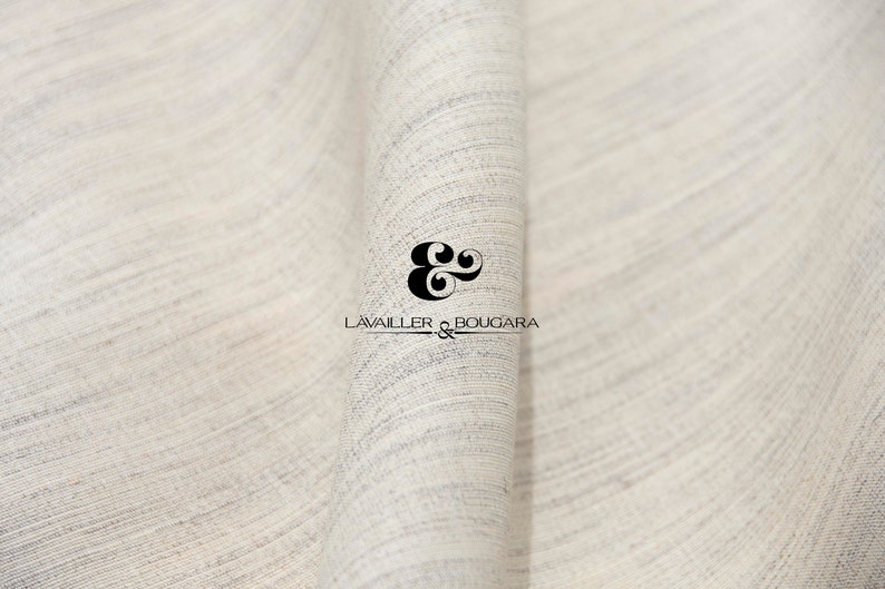 May include: Close-up of a white fabric with a subtle texture. The fabric is folded in half, creating a soft curve. The text "LAVAILLER & BOUGARDA" is printed in black on the fabric.