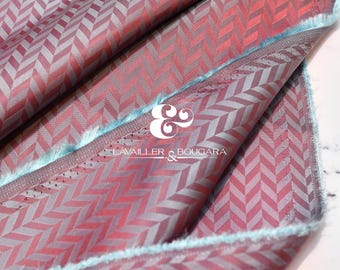 May include: Close-up of a folded fabric with a repeating chevron pattern in shades of red and gray. The fabric has a fringed edge and a logo that reads "LAVAILLER & BOUGARA".