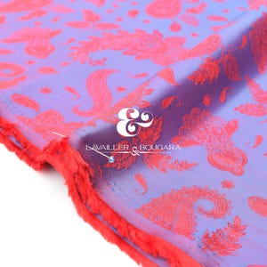 Puede incluir: Primer plano de una tela con un estampado de cachemira en tonos morados y coral. La tela tiene un borde sin rematar y deshilachado en coral. El texto "LAVAILLER & BOUGARA" es visible en la tela.