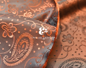 Könnte beinhalten: Nahaufnahme eines Stoffes mit Paisley-Muster in Braun- und Orangetönen. Der Stoff hat einen Satin-Glanz und ein detailliertes Blumendesign. Das Logo "AVALLER & BOUCARA" ist sichtbar.