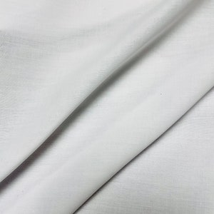 Puede incluir: Tela blanca con una textura lisa y uniforme. La tela está doblada por la mitad, creando un pliegue diagonal.