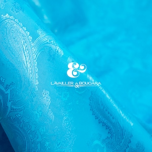 May include: A close-up of a turquoise blue fabric with a white paisley pattern. The fabric is folded over and the logo "LAVAILLE & BOUCARA" is visible in the center of the image.