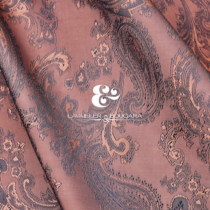 May include: A close-up of a brown fabric with a paisley pattern. The fabric has a subtle sheen and a soft texture. The text "LAVAILLEUR & BOUCARA" is printed in white on the fabric.
