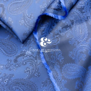 May include: Blue paisley patterned fabric with a textured surface. The fabric is folded and the edges are frayed. The text "LAVAILER & BOUGARA" is visible in the center of the image.
