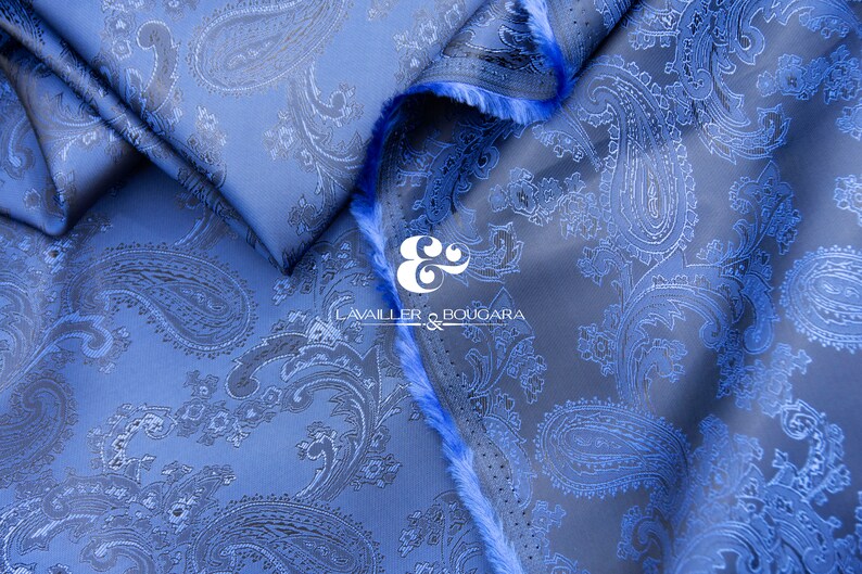 May include: Blue paisley patterned fabric with a textured surface. The fabric is folded and the edges are frayed. The text "LAVAILER & BOUGARA" is visible in the center of the image.