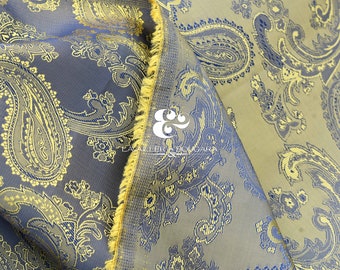 May include: A close-up of a fabric with a paisley pattern in shades of blue, gold, and brown. The fabric has a textured surface and a fringed edge.