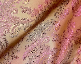 Könnte beinhalten: Nahaufnahme eines Stoffes mit Paisley-Muster. Der Stoff ist hellbraun mit einem pinkfarbenen und goldenen Metallic-Garn, das in das Design eingewebt ist.