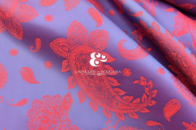 Puede incluir: Primer plano de una tela morada con un estampado de cachemira rojo. La tela tiene un brillo satinado y est&aacute; doblada, creando sombras y reflejos. El texto "LAVAILLER & BOUGARA" es visible.