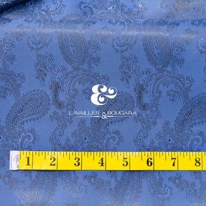 May include: Blue paisley fabric with a black paisley pattern. A yellow measuring tape is placed on the fabric, showing measurements from 1 to 10 inches.