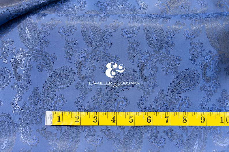 May include: Blue paisley fabric with a black paisley pattern. A yellow measuring tape is placed on the fabric, showing measurements from 1 to 10 inches.