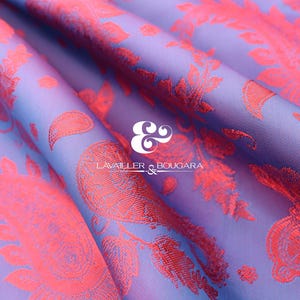 Puede incluir: Primer plano de una tela doblada con un estampado de cachemira. La tela tiene un fondo lavanda con un degradado de azul. El dise&ntilde;o de cachemira es de color coral brillante. El texto "LAVALLER & BOUGARA" es visible.