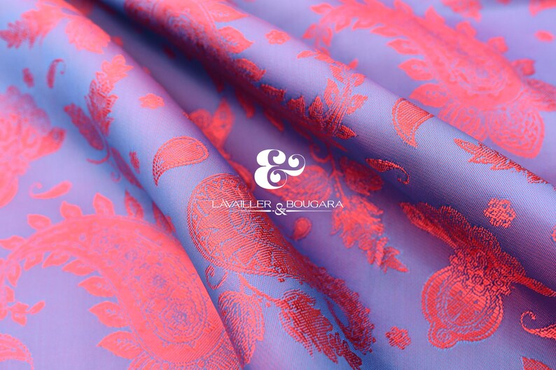 Puede incluir: Primer plano de una tela doblada con un estampado de cachemira. La tela tiene un fondo lavanda con un degradado de azul. El dise&ntilde;o de cachemira es de color coral brillante. El texto "LAVALLER & BOUGARA" es visible.