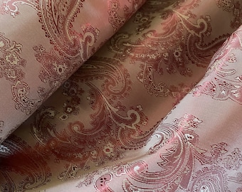 May include: Pink paisley patterned fabric with a subtle sheen. The fabric has a repeating pattern of paisley shapes in a darker shade of pink.